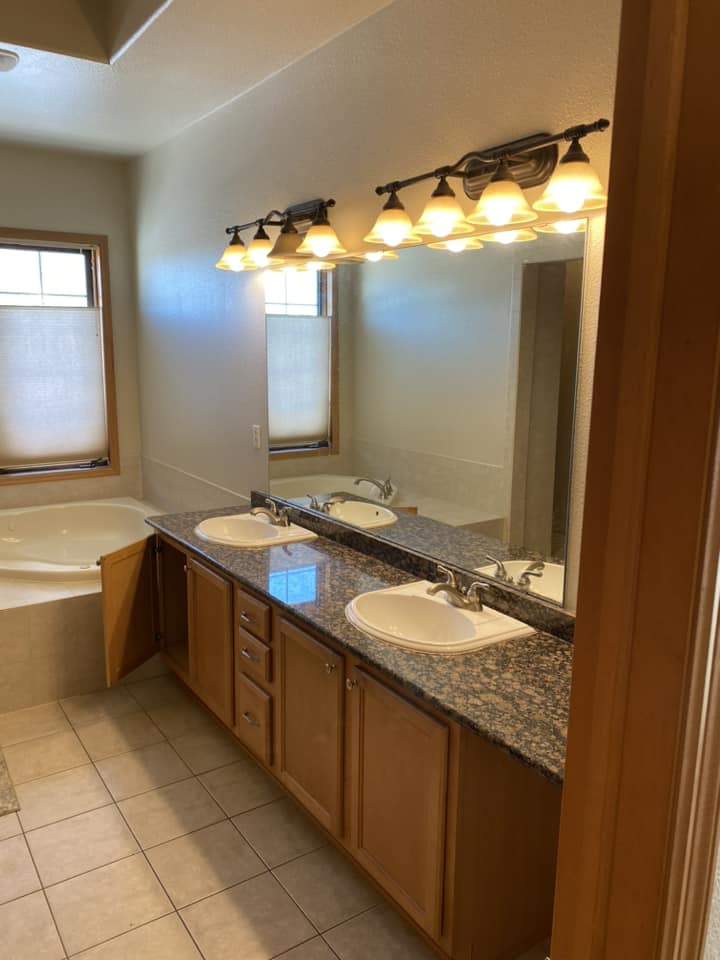Existing master bathroom before renovation with double-sink vanity, dark granite countertop, and jetted soaking tub
